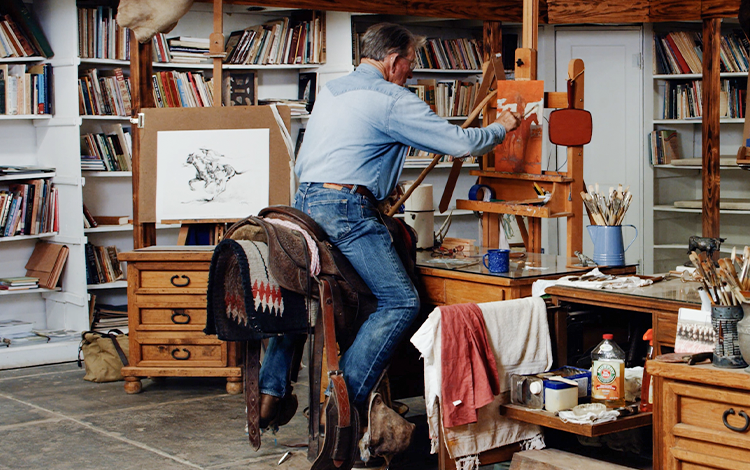 Mike sitting on saddle in studio, painting 